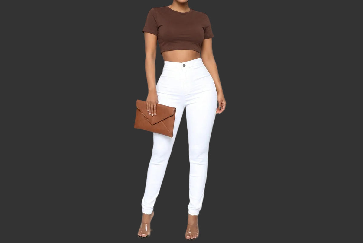 White high-waisted skinny jeans modeled with a white crop top and clear high-heeled sandals against a solid black background.