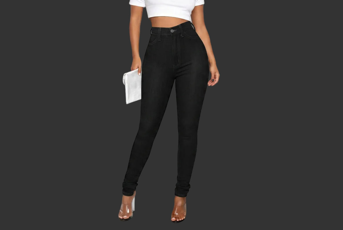 A model wearing high-waisted black skinny jeans, styled with a black crop top and clear high-heeled sandals, holding a white clutch against a plain white background.