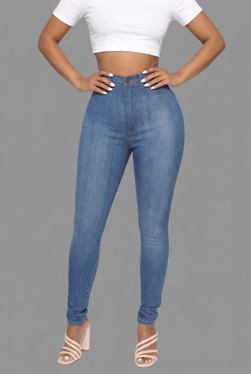 A model wearing high-waisted, skinny blue jeans, a white crop top, and white strappy heels against a plain white background.