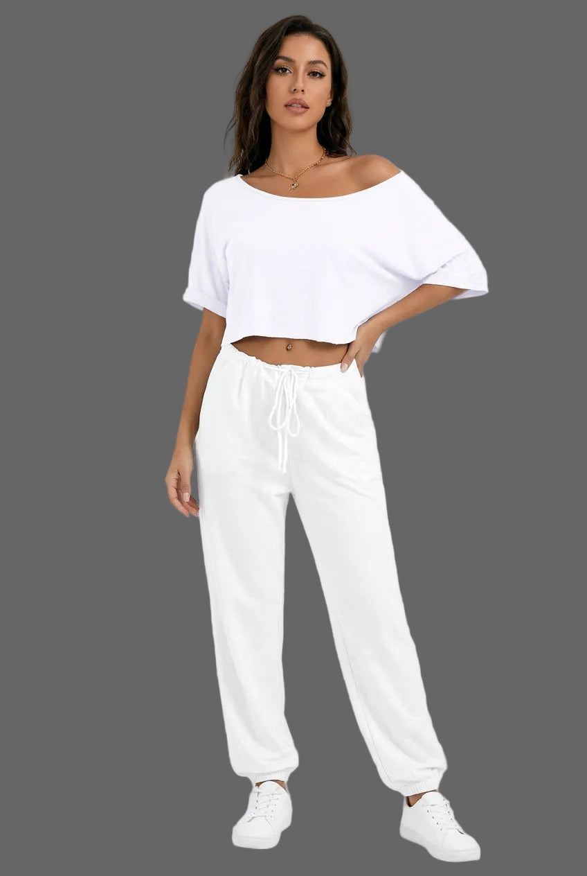 A woman wearing a white off-the-shoulder short-sleeve crop top and white drawstring pants against a plain gray background.