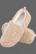 A pair of beige sherpa fleece slip-on slippers with a soft white lining and a small brown leather brand tab on the side, shown on a clean gray background.
