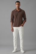 A man wearing a brown ribbed long-sleeve polo shirt with rolled-up sleeves and white pants