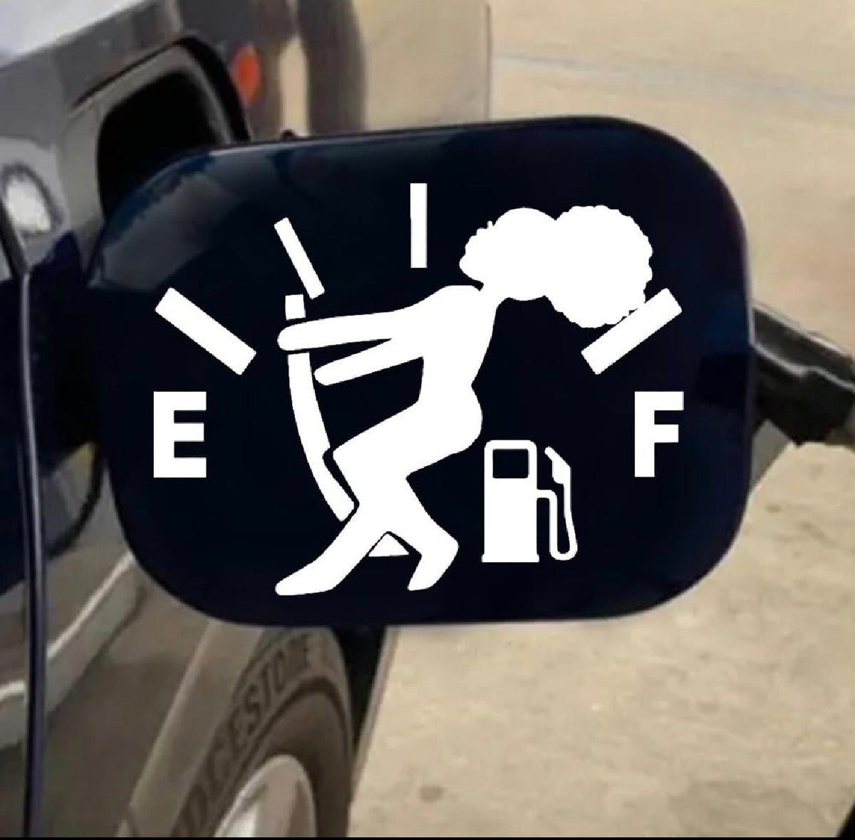 A white vinyl decal of the fuel gauge warning symbol with 'E' and 'F' letters and a gas pump icon, shown applied to a black vehicle fuel door.