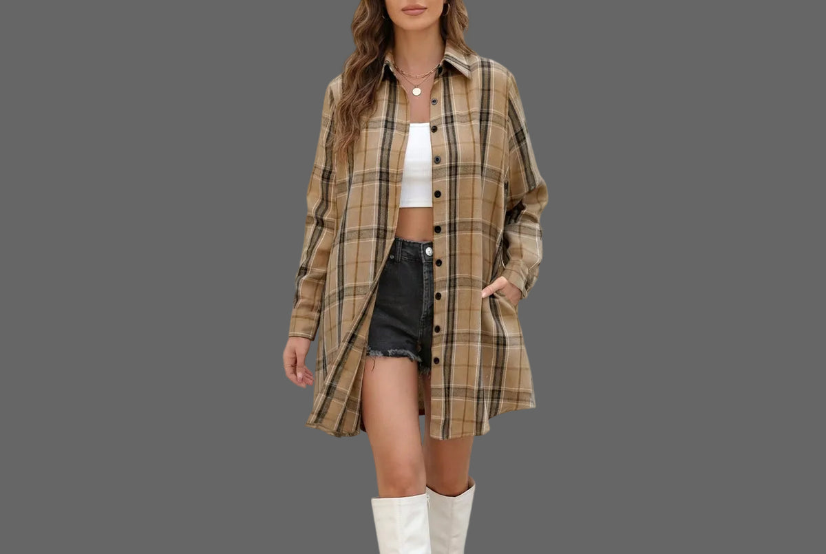 A woman wearing a beige and brown plaid button-up shirt over a white crop top and black denim shorts, photographed against a plain gray background.